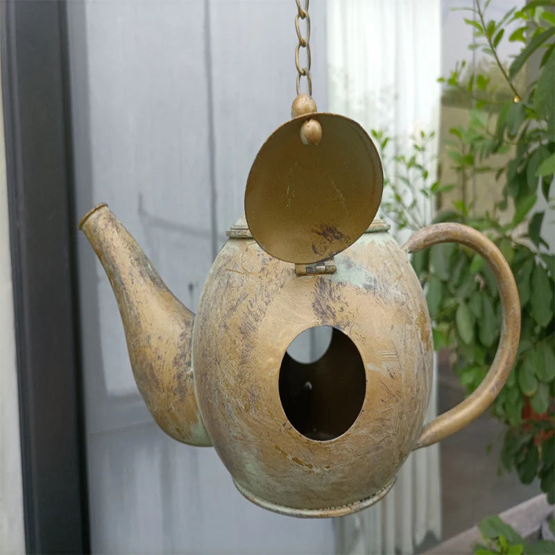 Decorative teapot birdhouse hanging outdoors with plants in the background