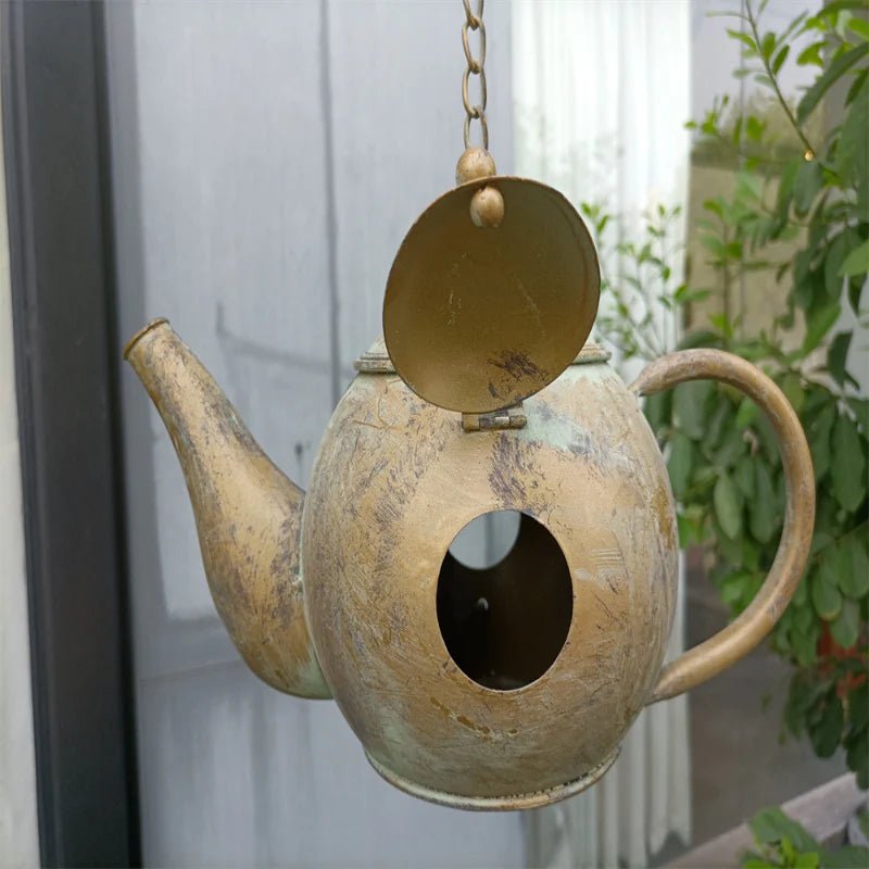 Bronze-gold teapot bird feeder with hanging chain, decorative lid, and large oval opening.