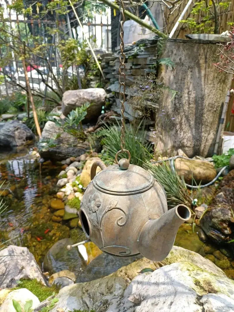 Decorative teapot in a garden setting with rocks and water