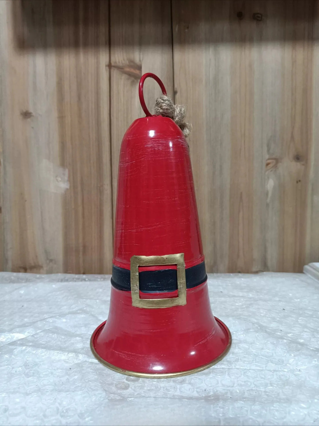 Red metal Santa bell decoration on a pedestal base with jute rope handle.