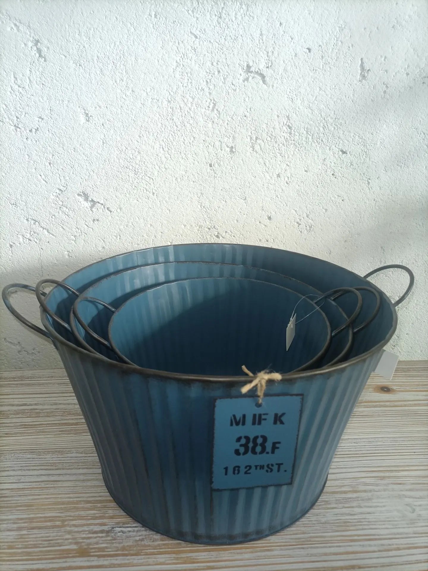 Set of three blue metal buckets on a wooden surface with a white wall background