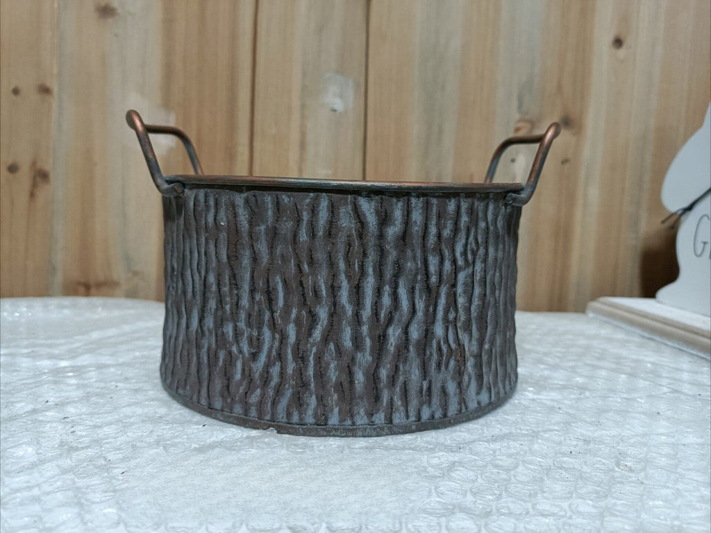 Textured metal basket with handles on a white surface with wooden background