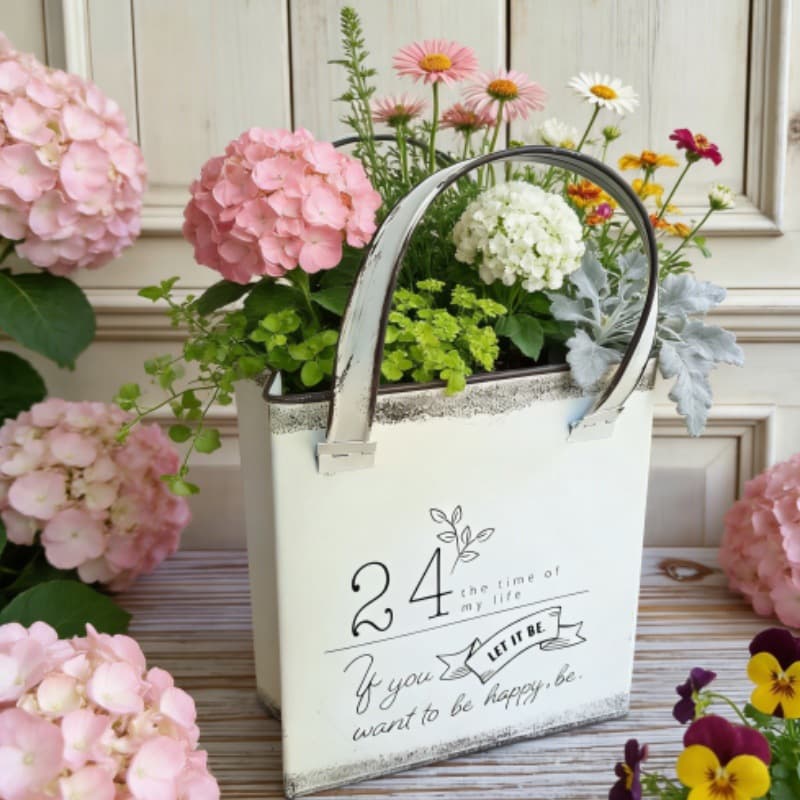 Decorative metal bucket with flowers and a motivational quote on a wooden surface.
