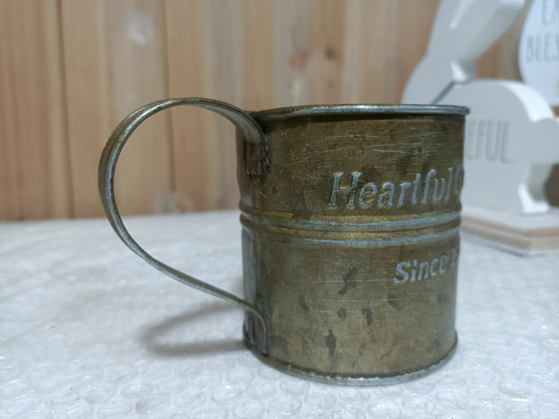Vintage-style metal mug with 'Heartful' and 'Since' text on a textured surface.