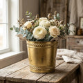 Antique gold distressed metal planter holding white flowers with green eucalyptus leaves