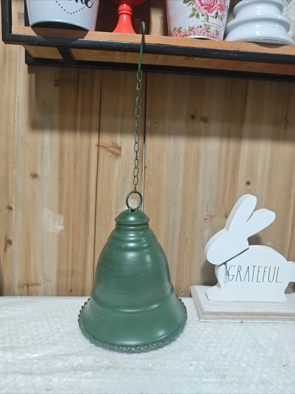 Green vintage iron hanging bell with chain, shown on shelf display