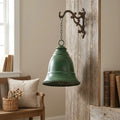 Green iron hanging bell with chain loop and domed shape against wood wall