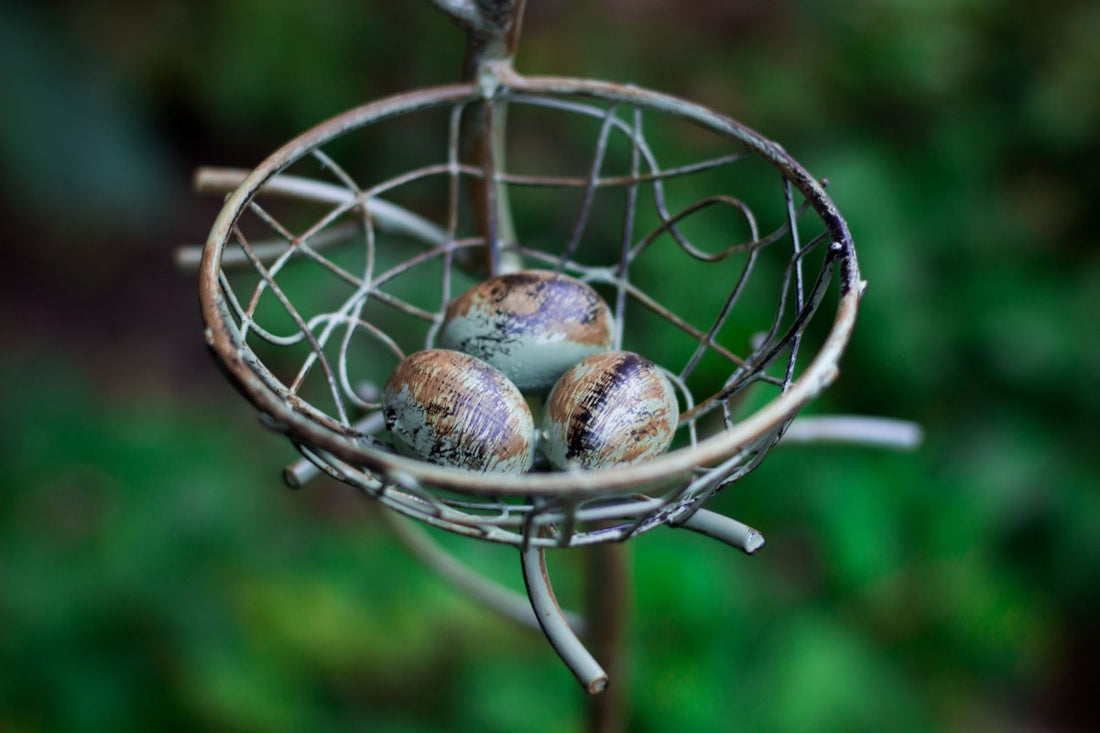 Round green wire nest basket filled with three egg-like pieces on a metal stake