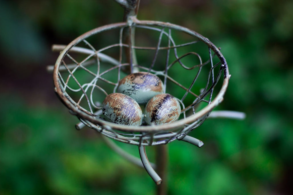 Round green wire nest basket filled with three egg-like pieces on a metal stake