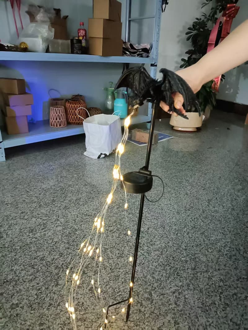 Lámpara de estaca con forma de dragón negro y guirnalda de luces cálidas en una habitación interior.