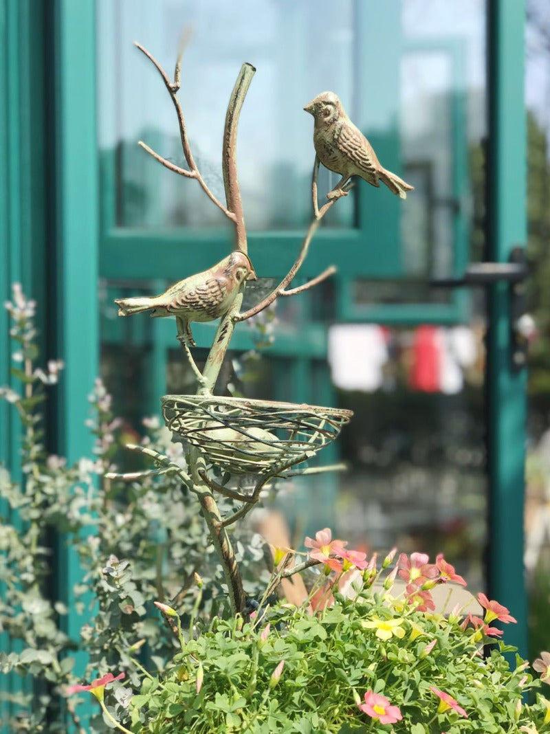 Metal bird nest garden stake trellis with two birds perched over a round wire nest, green finish