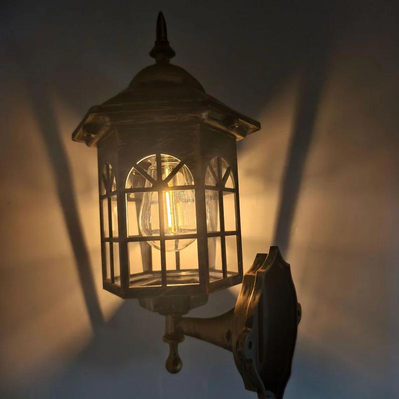 Bronze solar wall lantern with clear glass panels emitting warm light