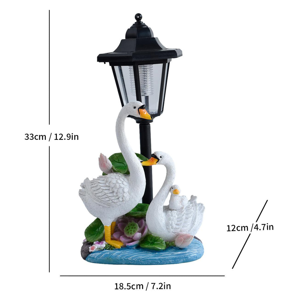 Solar garden animal statue with black lantern and three white swans on a blue base with flowers.