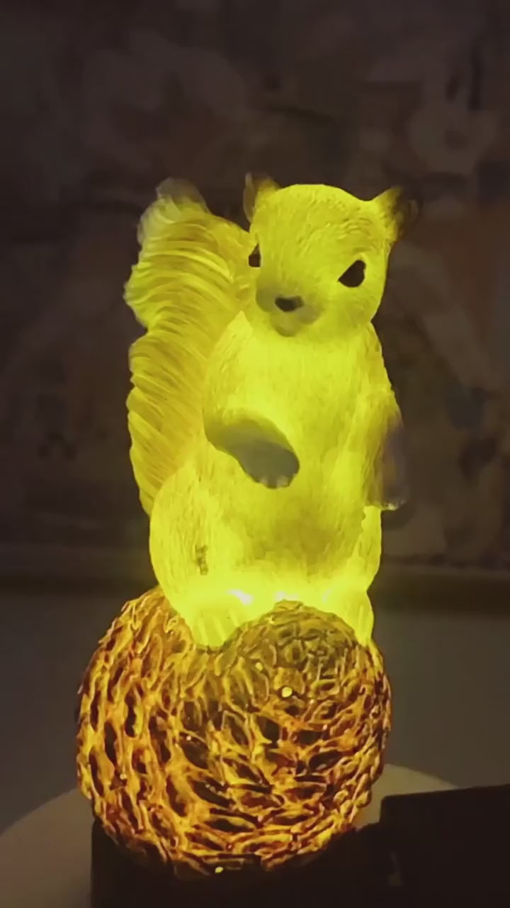 Short video showing a glowing resin squirrel garden light on a pinecone base illuminated with warm yellow light